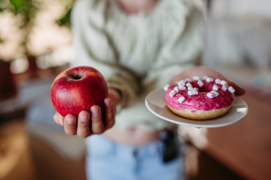 Diabetic woman is choosing between fresh apple and a sweet doughnut. Importance of proper nutrition