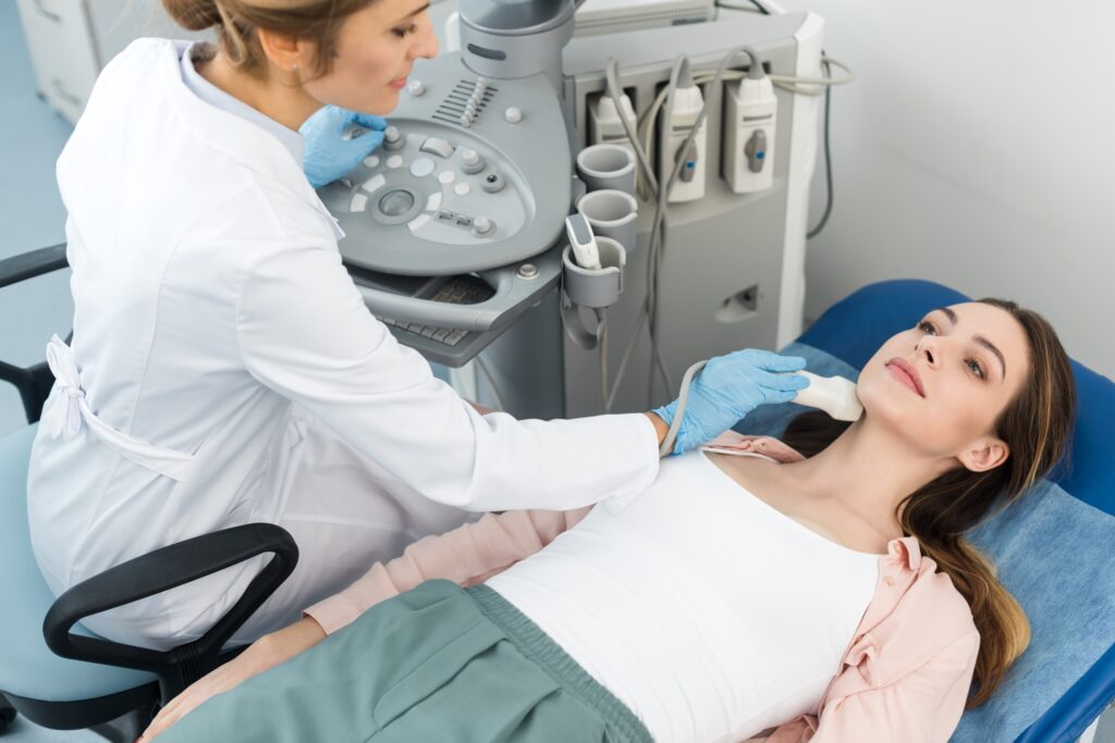 doctor examining thyroid of young woman with ultrasound scan in clinic
